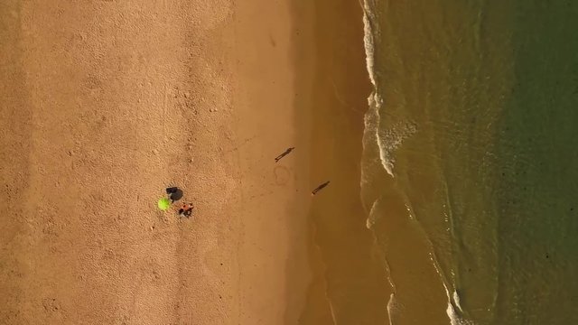 VERTICAL Aerial. ZOOMING OUT. Quiet sandy beach with rippling waves.