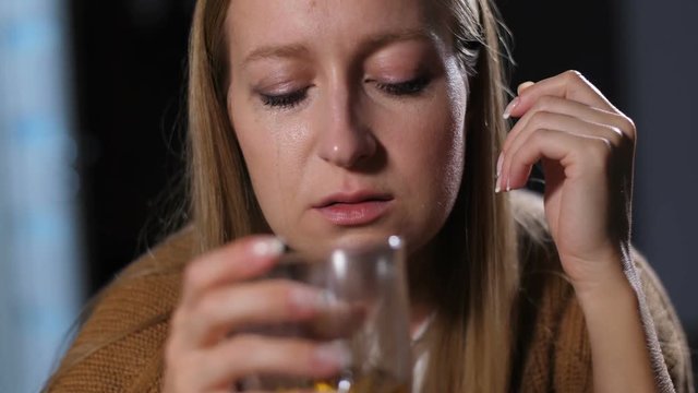 Drunk adult female feeling dizzy after too much alcohol, holding glass of alcohol while drinking alone at home. Boozer woman lost the touch with the ground, diving in alcohol addiction and abuse.