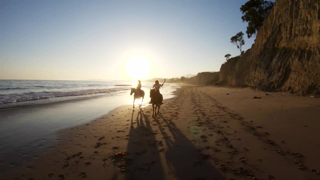 Women ride horses during sunset on beach, slow motion