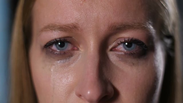 Closeup portrait of adult woman with deep sorrowful blue eyes staring into the distance as mascara runs down her face. Upset depressed female looking at camera, tears and makeup running down her face.