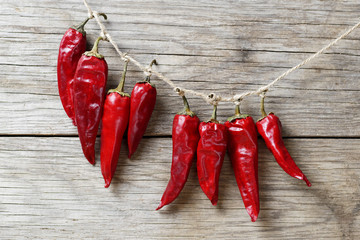 red chili peppers hanging and drying on a rope on a wooden wall