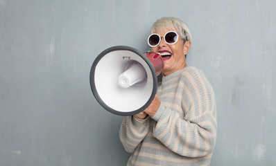 senior cool woman with a megaphone against grunge cement wall.