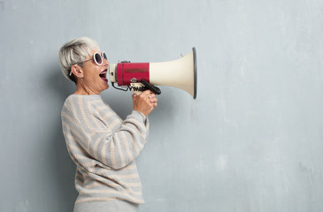 senior cool woman with a megaphone against grunge cement wall.