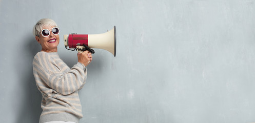 senior cool woman with a megaphone against grunge cement wall.