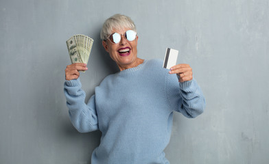 senior cool woman with a credit card against grunge cement wall. money or savings concept.