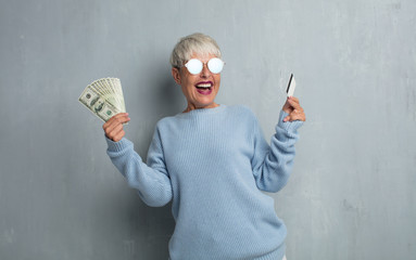 senior cool woman with a credit card against grunge cement wall. money or savings concept.