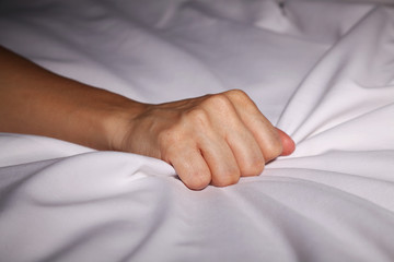 Woman's hand grabbing bed sheets during an orgasm