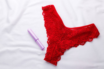 Sexy red panties and a tampon on a white blanket