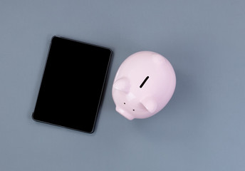 Traditional piggy bank and modern portable technology on gray desktop background
