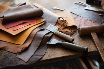 Deurstickers Leather craft or leather working. Selected pieces of beautifully colored or tanned leather on leather craftman's work desk . Piece of hide and working tools on a work table. © killykoon