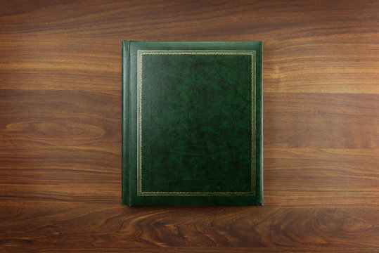 Green Photo album or Year book cover, blank, placed on a dark colored wooden table.