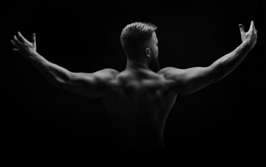 Obraz na płótnie Canvas Bodybuilder black and white portrait. Muscular man stands with his back and spread his arms to the side. Broad shoulders. Man unrecognizable