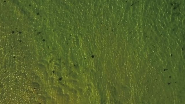 VERTICAL Aerial. MOVING BACKWARDS. Crashing small waves leading to calm green ocean.