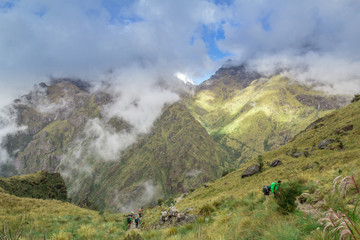 Obraz na płótnie Canvas Blue cloudy sky above verdant green mountains and hikers on the Inca Trail in Peru