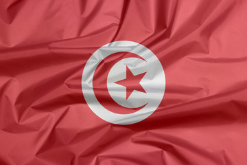 Obraz premium Fabric flag of Tunisia. Crease of Tunisian flag background, red and white flag with star and crescent in center.