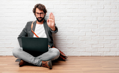 young man sitting on the floor Signaling stop with the palm of hand facing forward, with a serious...