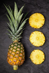 Fresh ripe pineapple and cut cross sections on dark background, vertical composition, top view