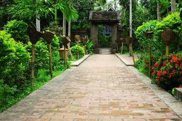 typical south east asian garden with lush vegetation with an old gate and torches along the pavement