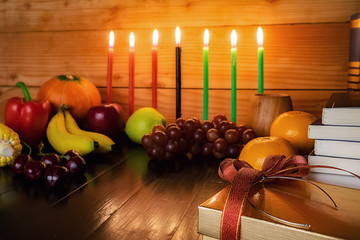Kwanzaa holiday concept with decorate seven candles red, black and green, gift box, pumpkin,corn and fruit on wooden desk and background.