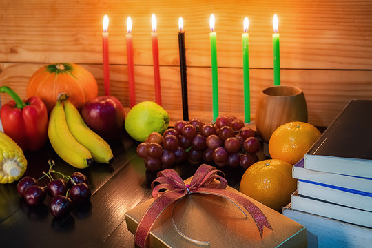 Kwanzaa holiday concept with decorate seven candles red, black and green, gift box, pumpkin,corn and fruit on wooden desk and background.