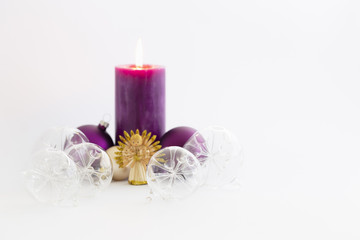 Obraz na płótnie Canvas Still life with beautiful decorative transparent christmas glass balls, a purple colored burning candle and a straw angel on white background