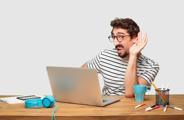 young bearded graphic designer with a laptop paying attention, trying to hear and listen to what is...