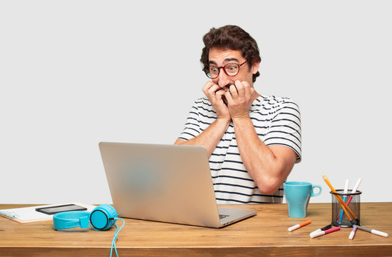 young bearded graphic designer with a laptop looking scared, frightened and horrified, screaming in terror, facing doom, feeling very afraid.