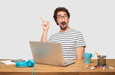 young bearded graphic designer with a laptop looking happy and surprised, smiling and thinking of...