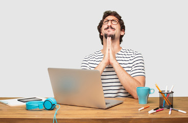 young bearded graphic designer with a laptop praying in a saintly manner, begging 