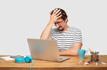 young bearded graphic designer with a laptop with a sad look of disappointment and defeat, looking...