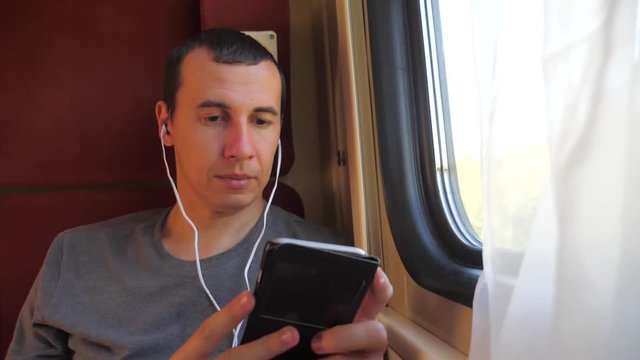 man listening to the music on the train rail car coupe compartment travel. slow motion video. man with a smartphone at the window of a train in lifestyle a car travel internet social media web. man