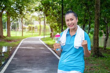 Asian woman relax time after jogger in park.She is show hand and show good .She is hold water bottle after drinking water. Life style, Photo concept  exercise and healthy.