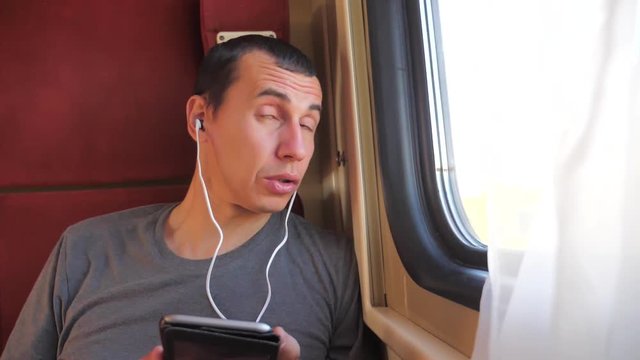 man listening to lifestyle the music on the train rail car coupe compartment travel. slow motion video. man with a smartphone at the window of a train in a car travel internet social media web. man