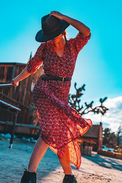 Girl with hat and red dress dancing in the desert