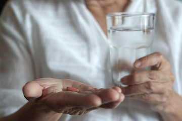 elderly woman are  eating medicine and with pills and glass of water at home