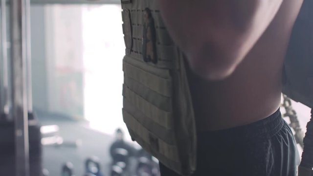 Muscular guy putting on a military looking weight vest before training.
