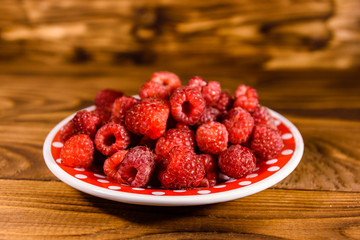 Ceramic plate with ripe raspberries on wooden table