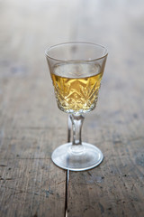 Glass of white wine in a antique glass, placed on a old wooden table.
