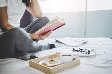 Young woman happiness on bedroom in enjoying reading books and newspaper in holiday with morning coffee, relaxation and recreation concept
