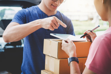 Woman customer appending signature in digital tablet and receiving a cardboard boxes parcel from...