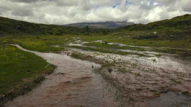 Time-lapse of muddy floodwater running over the paramo. Cotopaxi Volcano, partially hidden in the clouds in the distance. In the Andes, Ecuador.