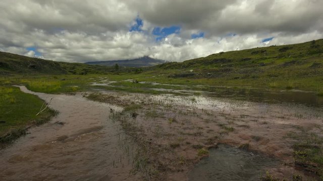 Time-lapse of muddy floodwater running over the paramo. Cotopaxi Volcano, partially hidden in the clouds in the distance. In the Andes, Ecuador.