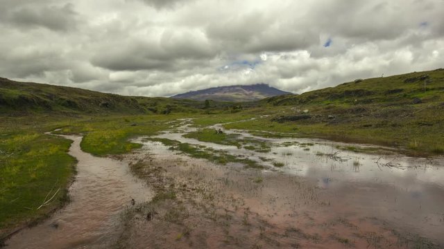 Time-lapse of muddy floodwater running over the paramo. Cotopaxi Volcano, partially hidden in the clouds in the distance. In the Andes, Ecuador.
