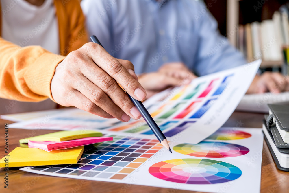 Poster Two colleague creative graphic designer working on color selection and color swatches, drawing on graphics tablet at workplace with work tools and accessories