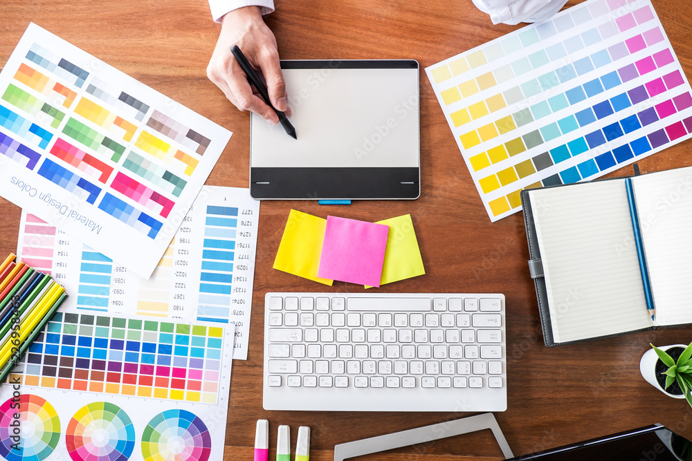 Poster Image of male creative graphic designer working on color selection and drawing on graphics tablet at workplace with work tools and accessories, top view