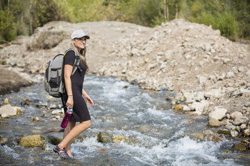 Obraz premium Attractive Woman hiking across a shallow mountain stream while on vacation in the Western United States. Candid photo of an active female enjoying the outdoors