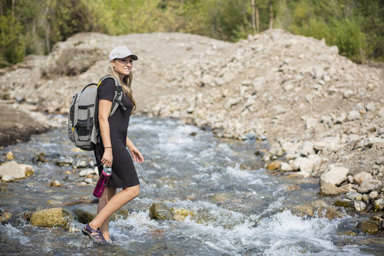 Attractive Woman hiking across a shallow mountain stream while on vacation in the Western United States. Candid photo of an active female enjoying the outdoors