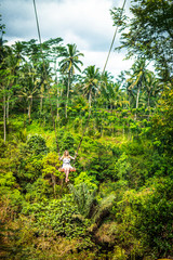 Fototapeta na wymiar Young tourist woman swinging on the cliff in the jungle rainforest of a tropical Bali island.