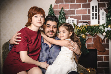 Family with Russian mom, Turkish dad and their daughter are in a room decorated for Christmas and new year