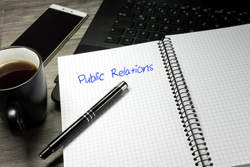 Ein Handy, Computer und ein Heft mit dem Wort Public Relations PR
